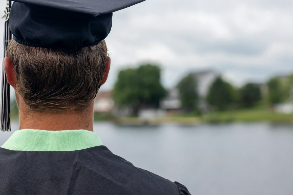woman in black academic dress and black cap standing near body of water during daytime